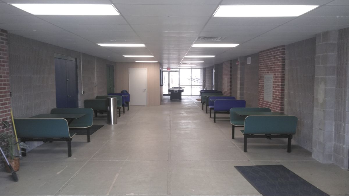 An empty lobby with several tables and chairs in it, and a foosball table and airhockey table in the background.