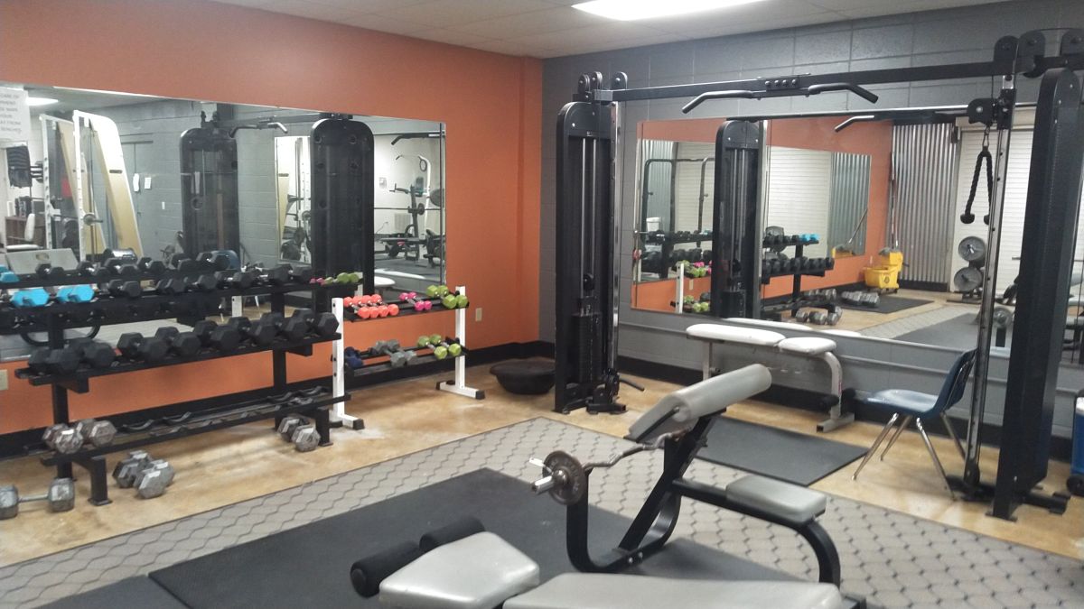 Set of weight racks and piece of weight lifting equipment with another in the front and mirrors in the background in a corner of Dell Gym's Weight room