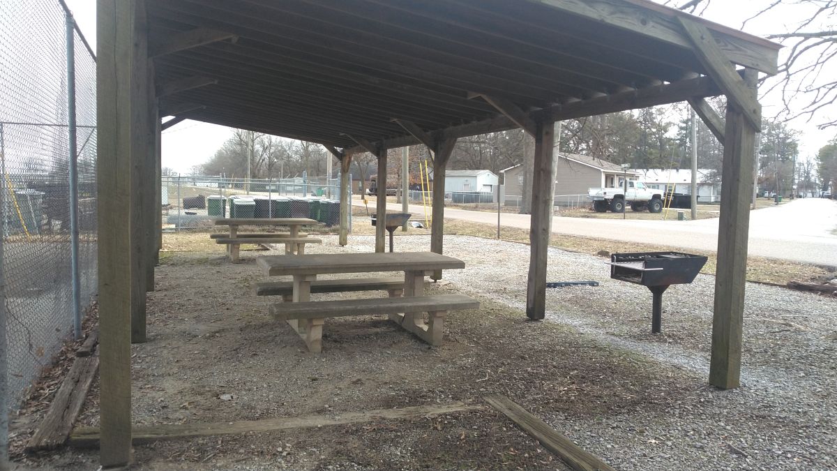 Wood pavillion with 2 sets of concrete picnic tables, benches, and grills beneath it next to the Tennis Court